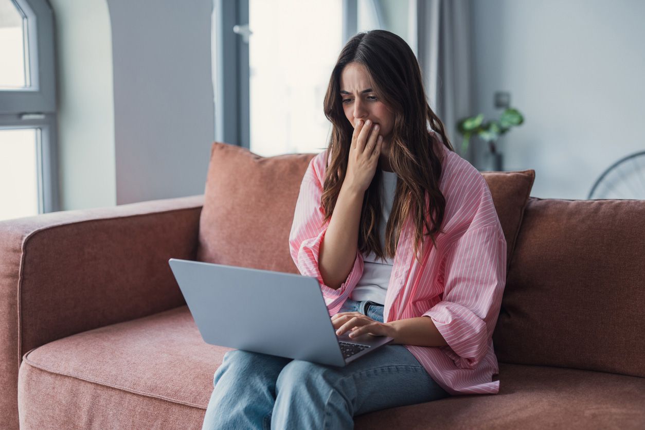 Woman looking concerned while reading a work message on her laptop at home